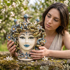 Woman looking at the Medusa head with flowers resting on a wall in an orchard
