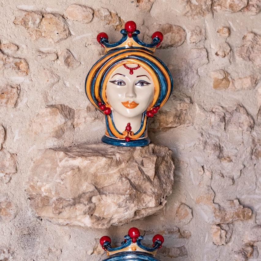 Weibliche Testa di Moro in Blau und Orange auf einem vorstehenden Stein einer rustikalen Mauer
