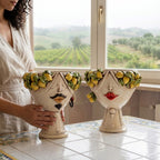 Pair of Zahira heads with lemons, man with moustache and woman, on a majolica table facing vineyards