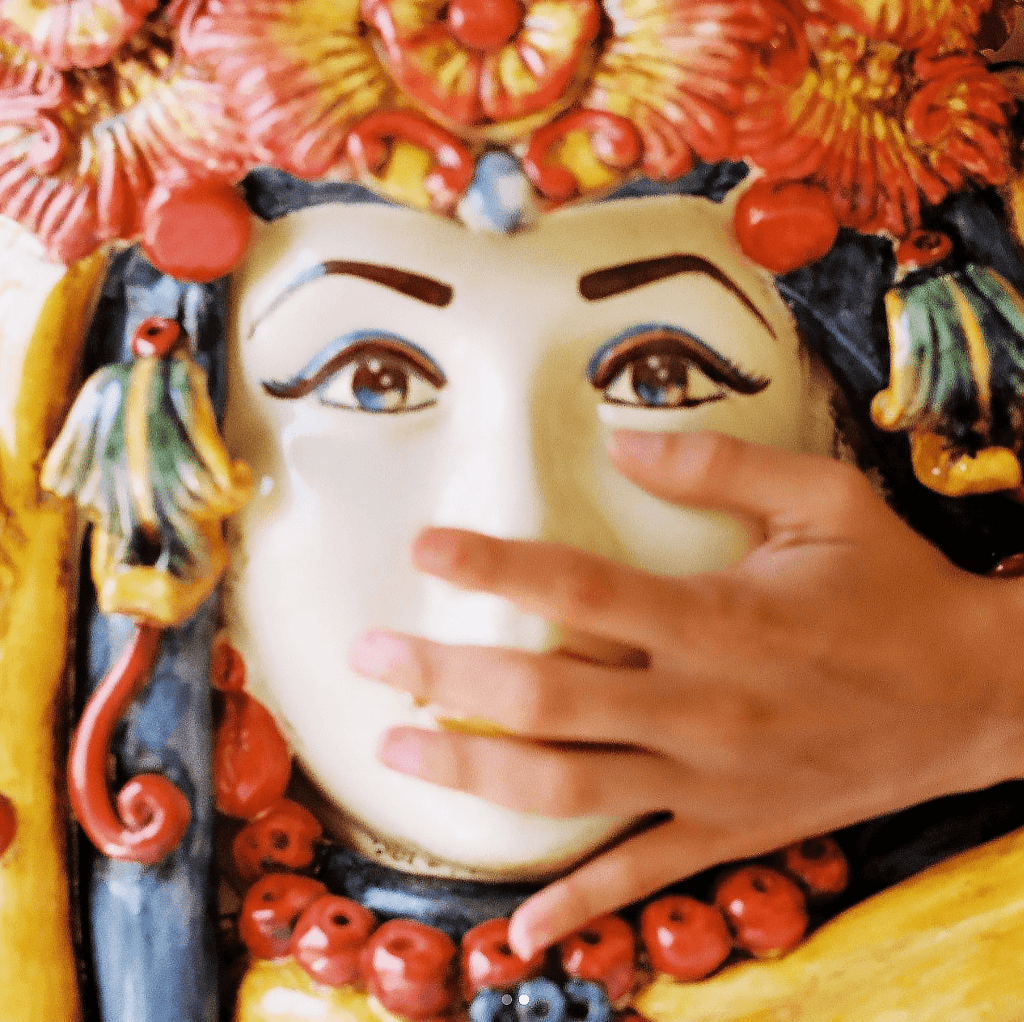 A hand touching the face of the 50 cm Testa di Moro with turban, hand-painted red and orange flowers